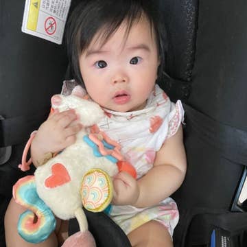 Baby sitting in a car seat holding a colorful toy