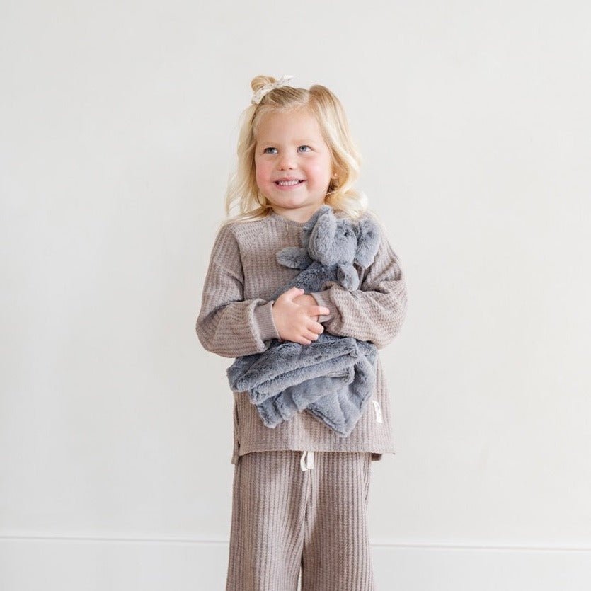 Child holding a gray elephant plush toy against a white background
