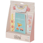 Love, Stella 12-month travel set in its original pink and white cardboard packaging, featuring a light blue fabric passport cover, a pastel bib, a yellow flower-shaped sunglasses holder, and a sticker sheet.