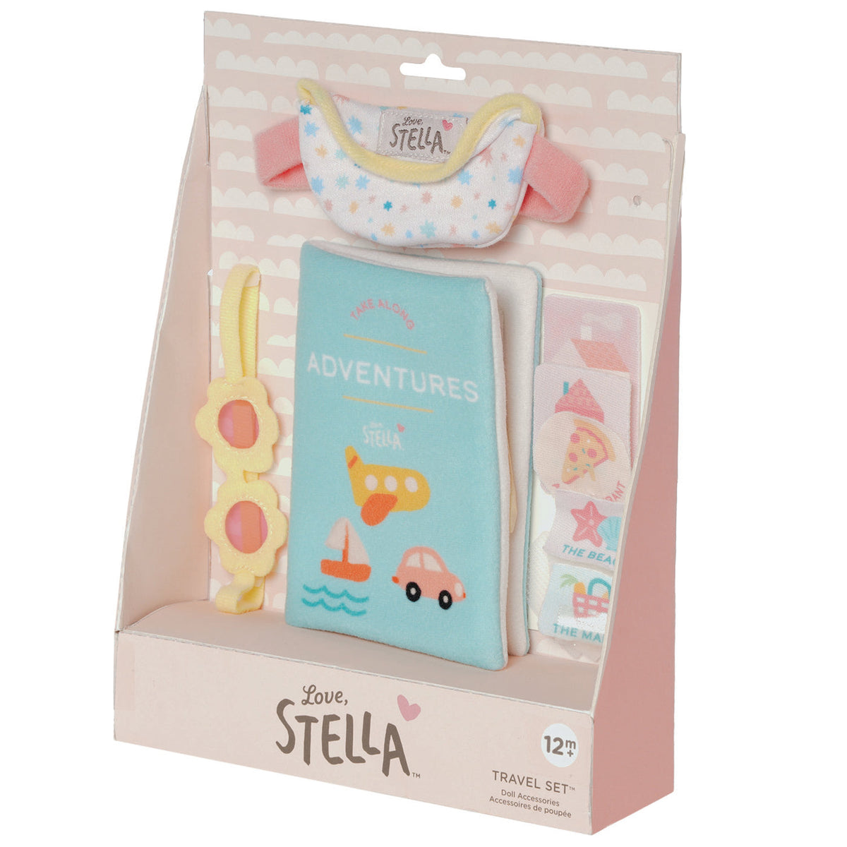 Love, Stella 12-month travel set in its original pink and white cardboard packaging, featuring a light blue fabric passport cover, a pastel bib, a yellow flower-shaped sunglasses holder, and a sticker sheet.