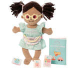 Doll with pigtails wearing glasses and a dress, accompanied by a book titled 'Adventures' on a white background.