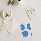 Stationery items including cards, an envelope, and a small dish with stamps on a light surface.