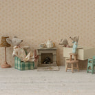 Miniature diorama with toy mice and furniture against a patterned wall.