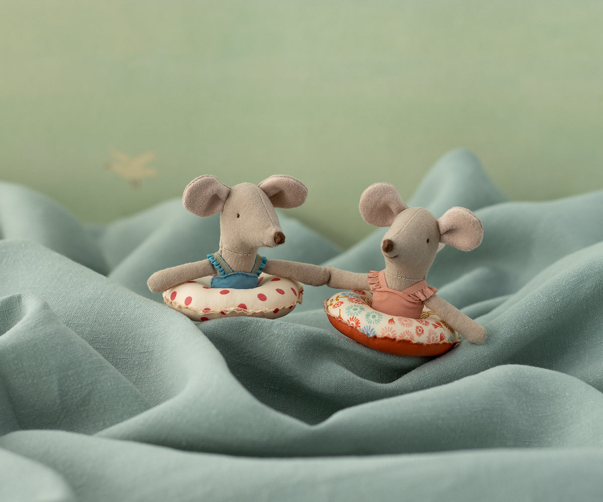 Two plush mouse toys on a textured surface with a soft green background
