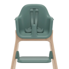 A high chair with a muted sage green molded plastic seat, straps, and footrest, supported by a light natural wood frame, shown from the rear on a white background.