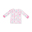 A long-sleeve children's top with a white base, featuring an all-over pattern of pink bows and light green pine trees, finished with solid pink cuffs.