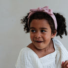 Young girl with a pink headband and white top against a plain background