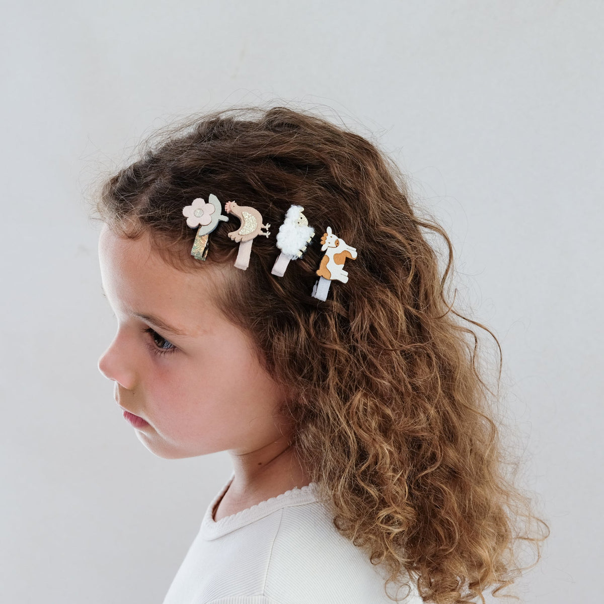 Child with curly hair wearing animal-themed hair clips against a plain background