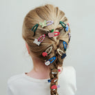Person with braided hair adorned with various colorful hair clips on a plain background