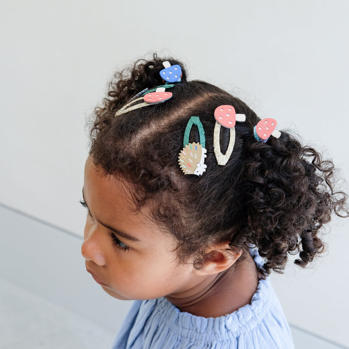 Child with curly hair wearing colorful hair clips against a light background