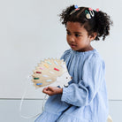 Child holding a colorful hedgehog-shaped bag against a light background