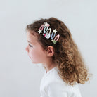 Child with curly hair wearing a decorative hair clip against a white background