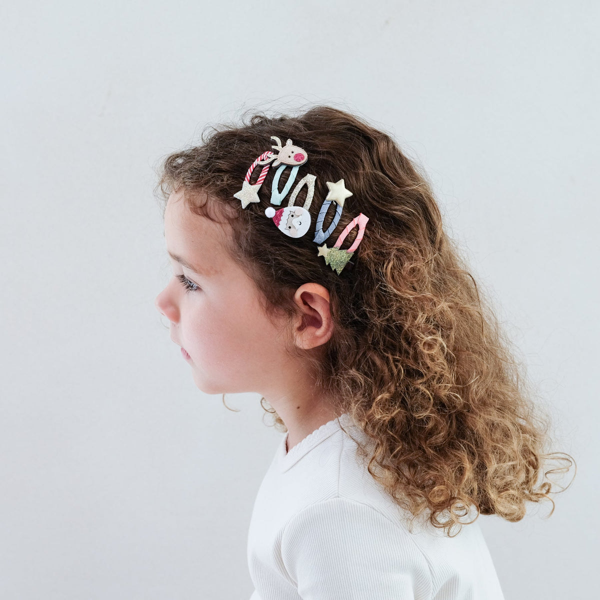 Child with curly hair wearing a decorative hair clip against a white background