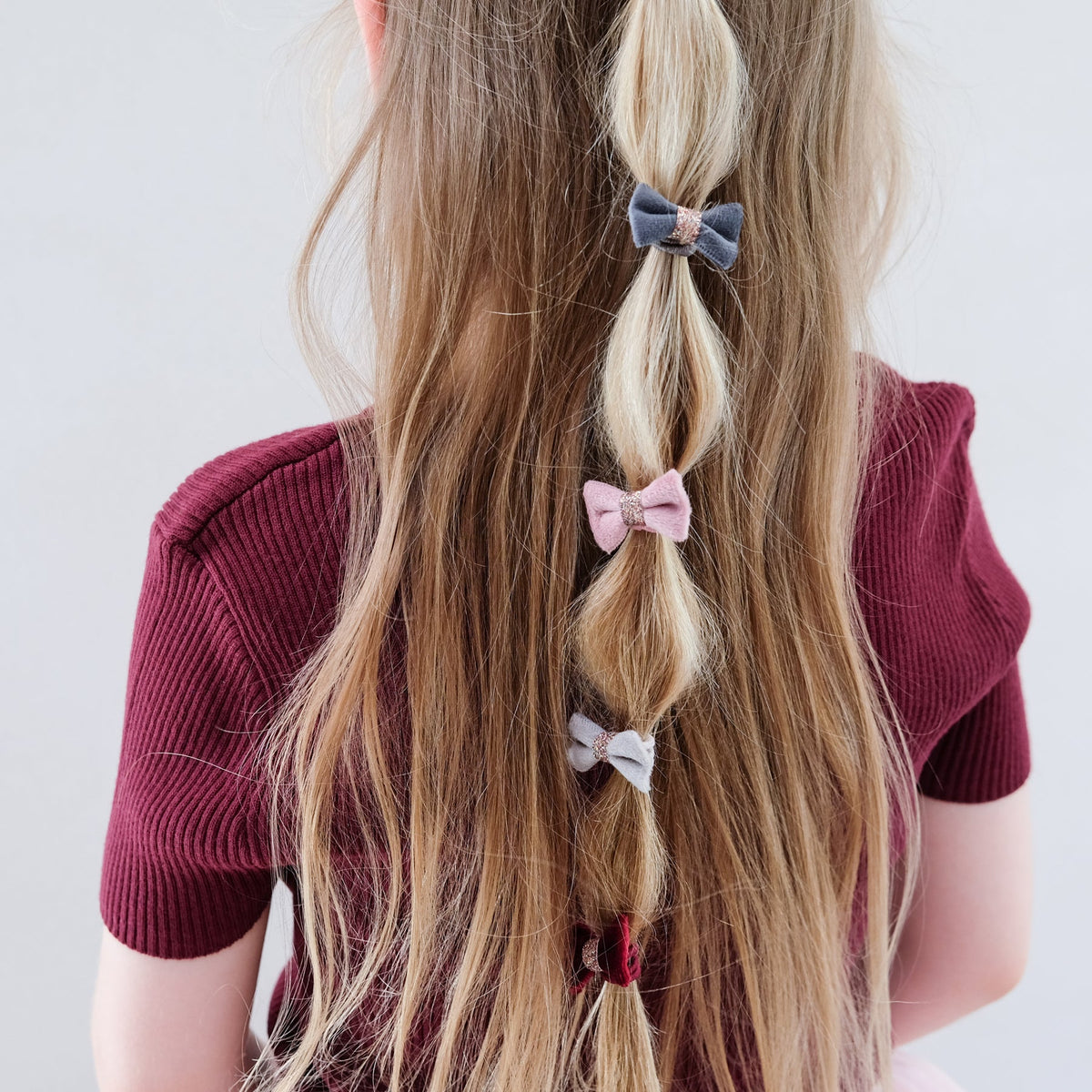 Person with long blonde hair styled in braids, wearing a maroon top on a white background