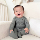 A baby wearing a gray long-sleeve footed sleeper with a small tree print