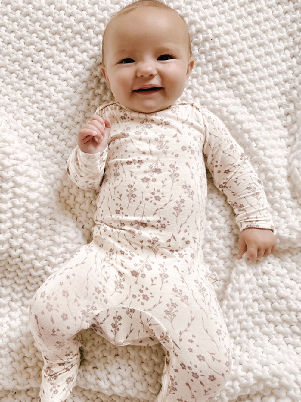 Baby wearing a floral onesie lying on a textured white blanket