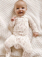 Baby wearing a floral onesie lying on a textured white blanket