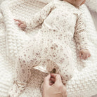Baby in a floral outfit lying on a soft, textured blanket with a hand adjusting the fabric.