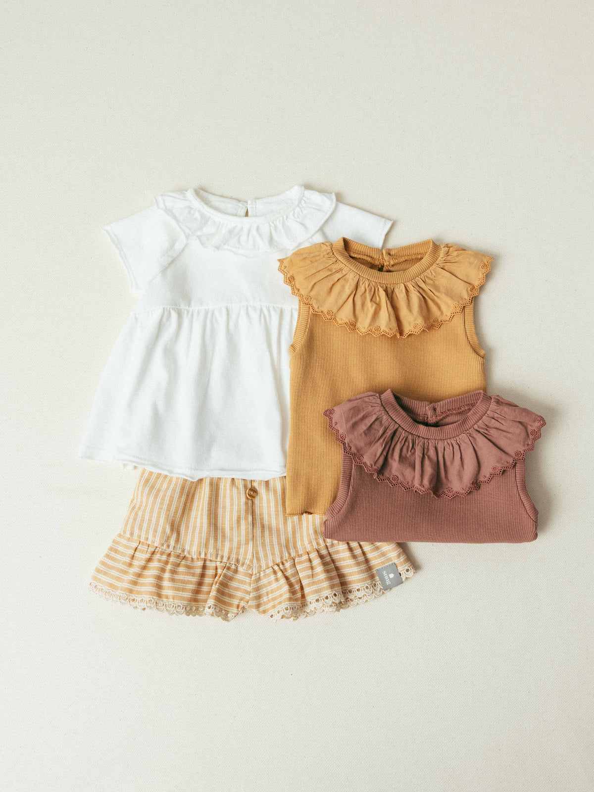 Three children's tops with ruffled details on a beige background