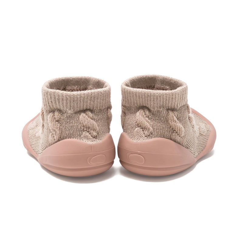 A pair of slip-on knit booties shown from the back, featuring a textured beige cable-knit upper and a dusty pink sole.