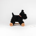 Black dog-shaped pull toy with wooden wheels on a white background