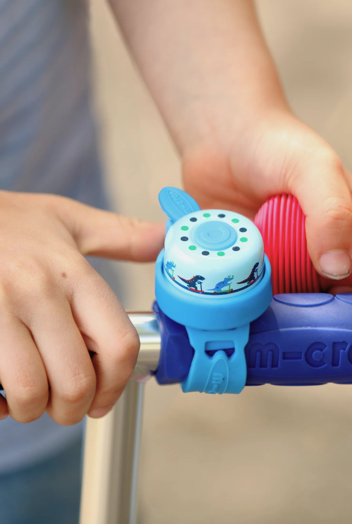 Child's hand holding a blue and purple bicycle bell on a bike handlebar.