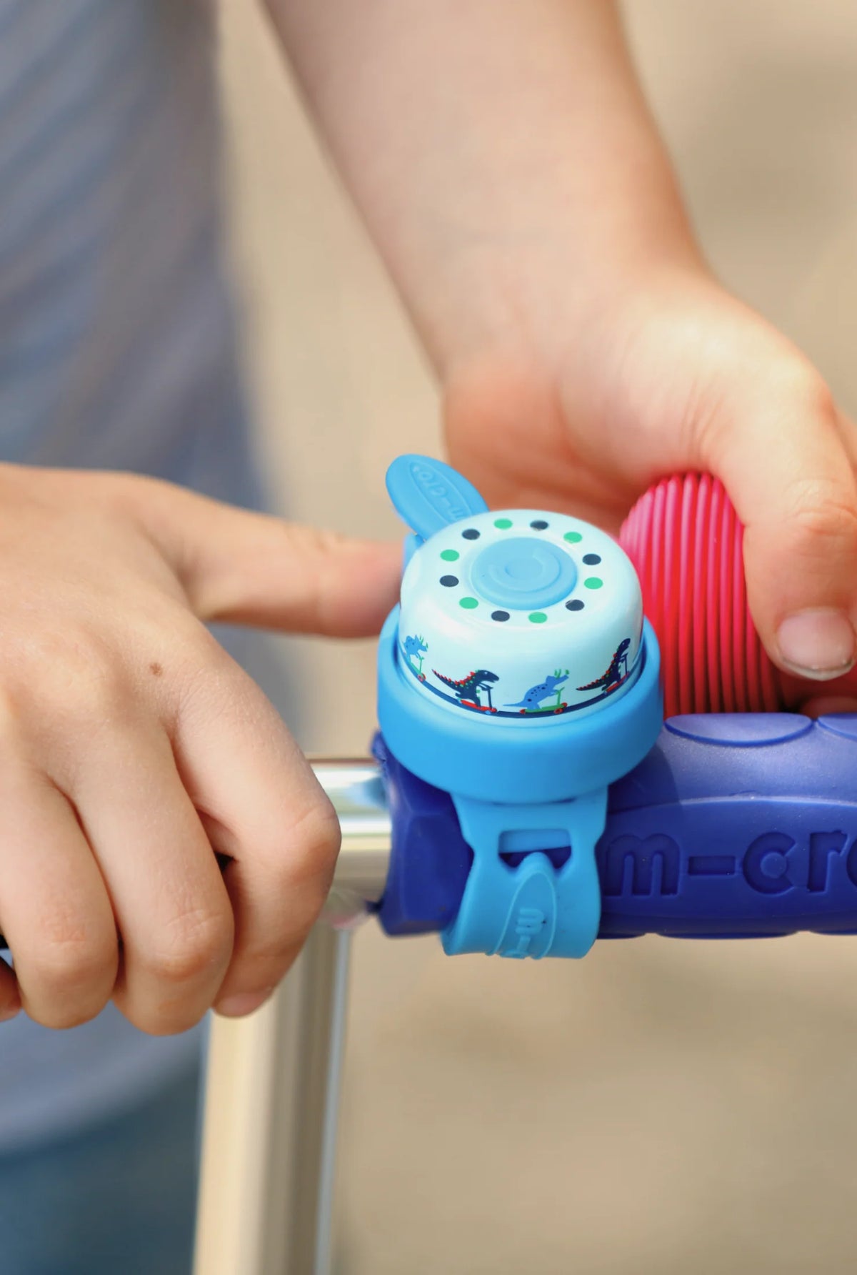 Child's hand holding a blue and purple bicycle bell on a bike handlebar.