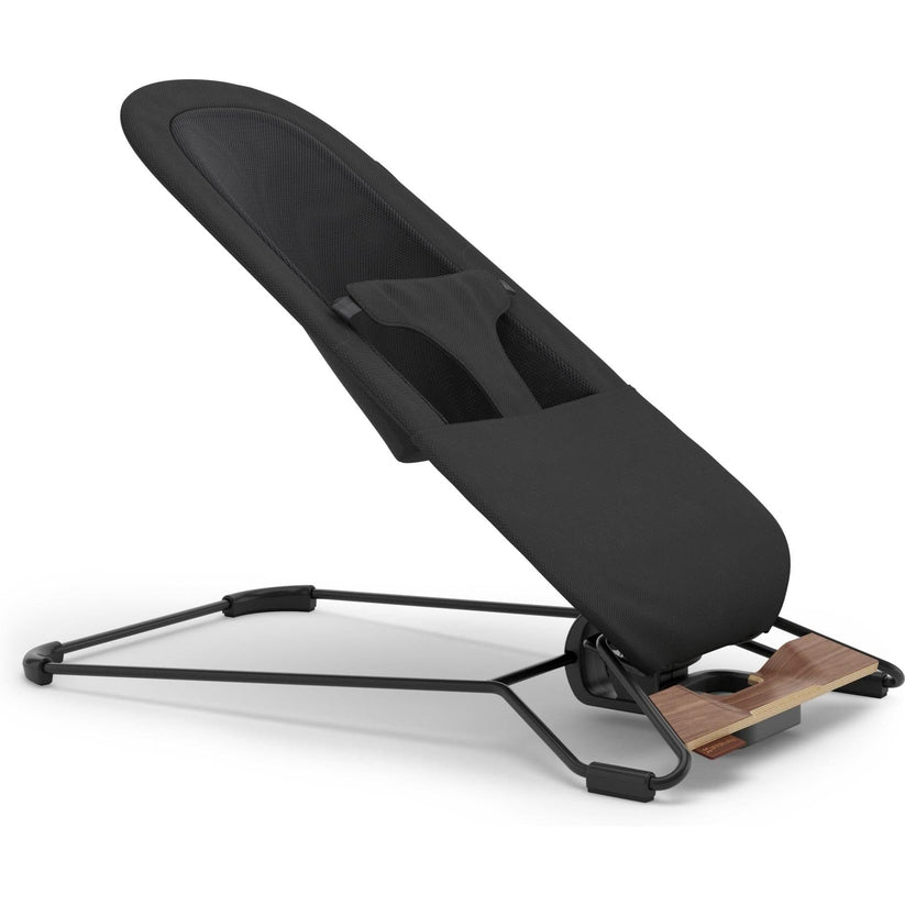 A modern black baby support seat with a black fabric liner, black metal frame, and a small wooden footrest, shown on a clean white background.