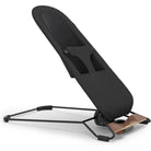 A modern black adjustable baby support seat with a minimalist black metal frame and a natural wood base, shown on a clean white background.