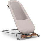 A modern baby support seat with a light beige fabric cushion, a breathable mesh back panel, and a dark gray metal frame with a wooden base, shown on a white background.