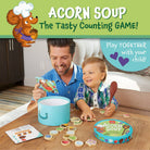 Man and child playing with 'Acorn Soup: The Tasty Counting Game' on a wooden table.