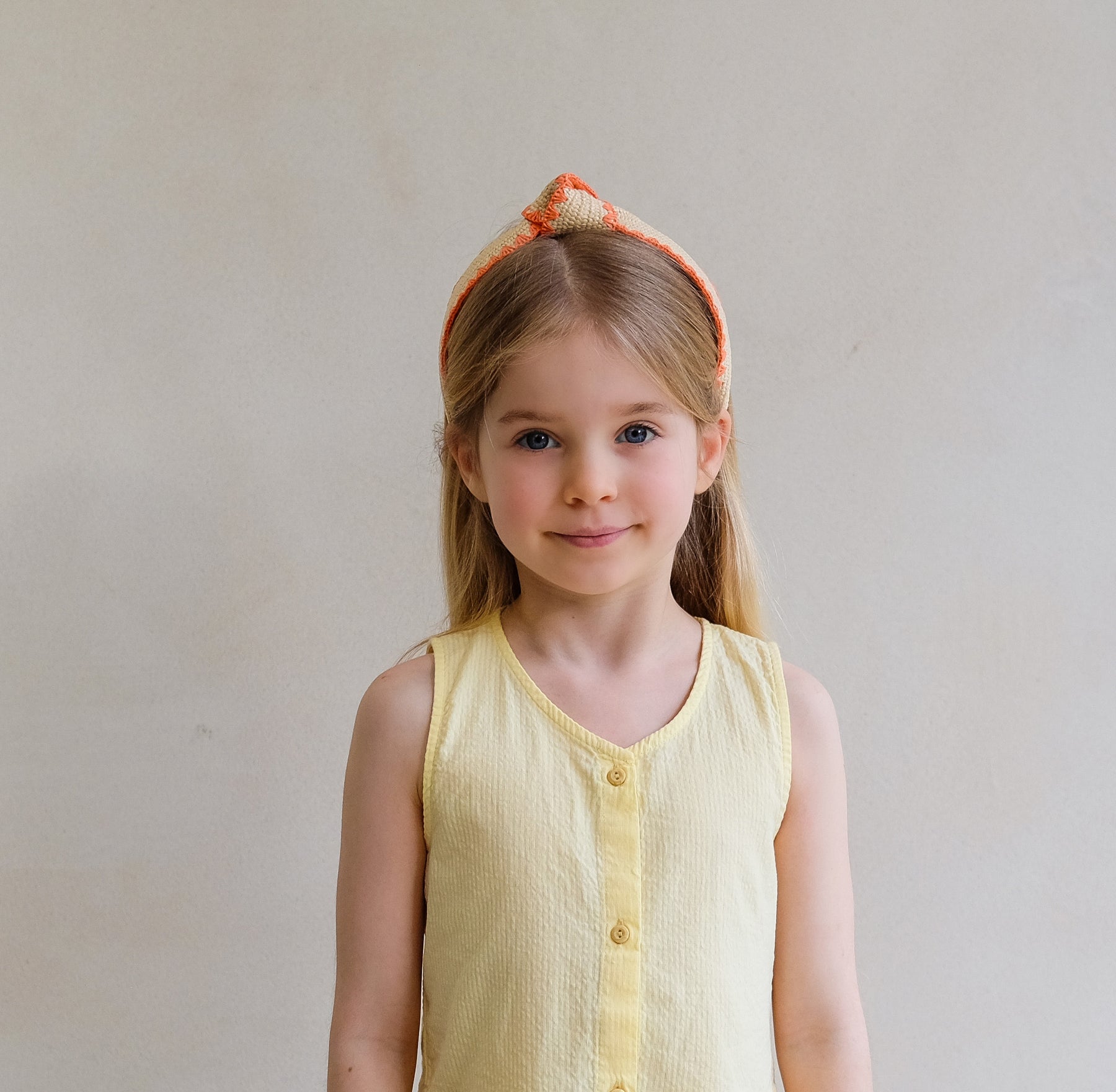 Young girl wearing a yellow sleeveless shirt with a plain background