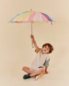 Child holding a colorful striped umbrella against a beige background