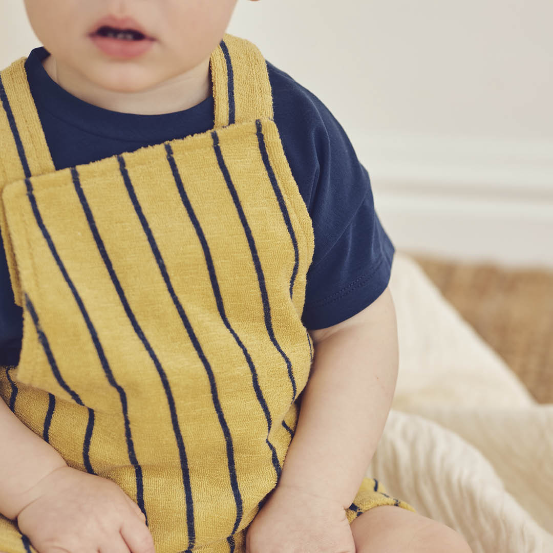 Child wearing a yellow striped apron over a blue shirt, sitting on a beige couch.