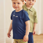Two young boys wearing navy and green shirts with matching pants indoors.