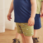 Children wearing navy shirts and green shorts with dog prints on a wooden floor.