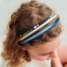 Three fabric headbands in blue, beige, and black with colorful floral and animal prints, worn by a young girl with curly brown hair.