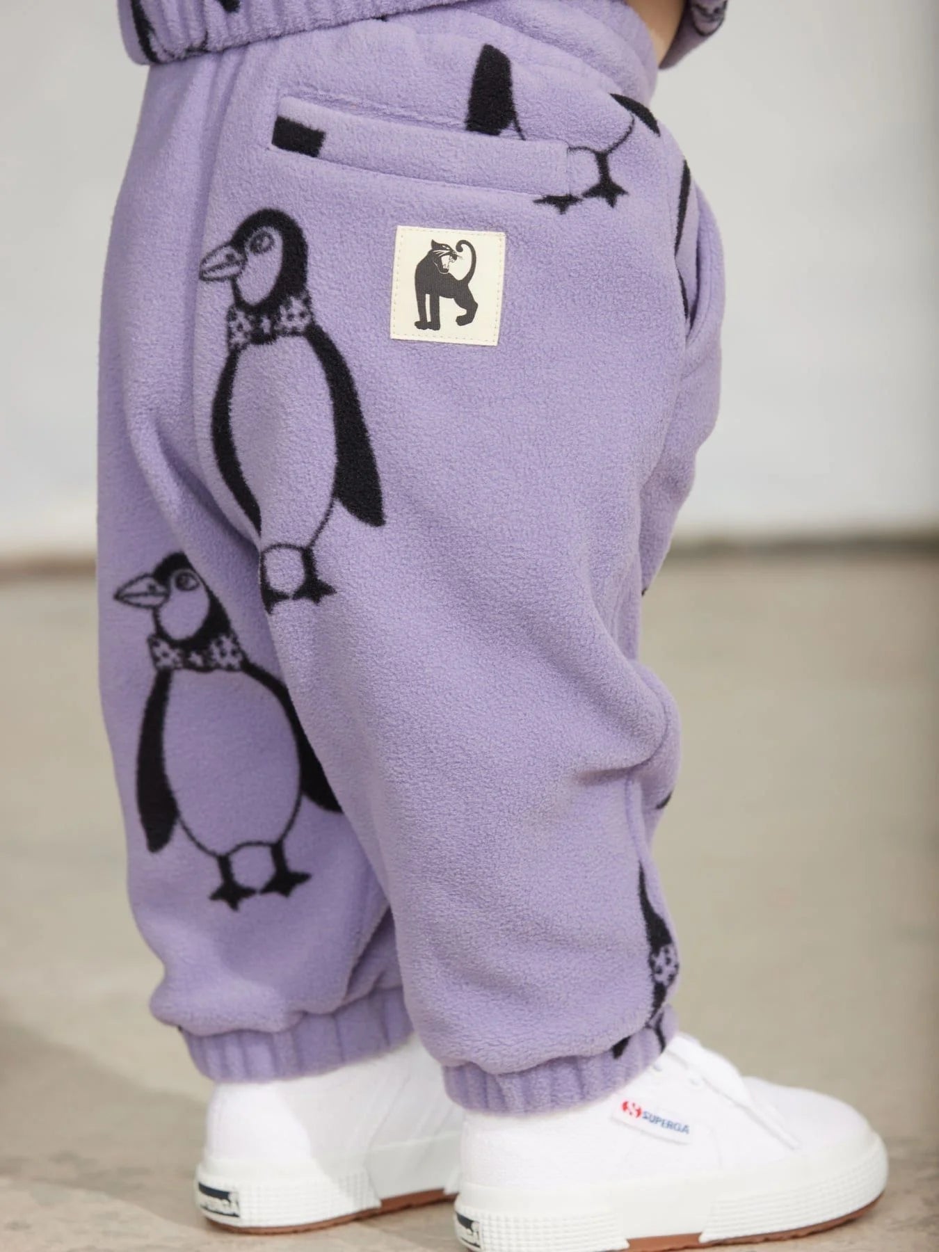 Close-up of a child wearing lavender fleece pants with black penguin prints and white sneakers.