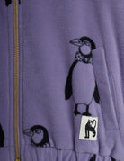 Close-up of a lavender fleece zip-up jacket featuring a black penguin print and a small white brand patch with a black cat silhouette.