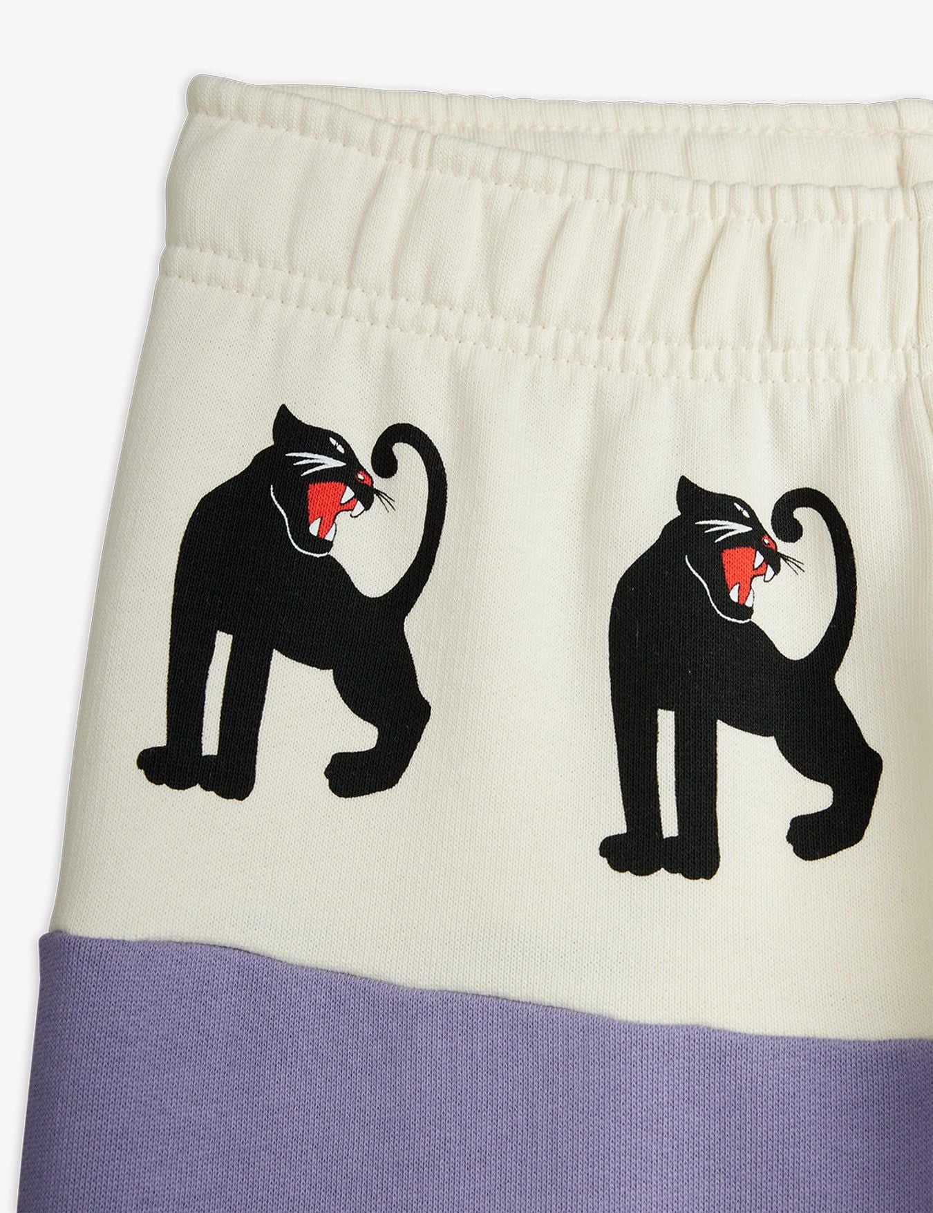 Close-up of a garment showing an off-white upper section with two black panther graphics holding red flags, and a lavender-purple lower band.