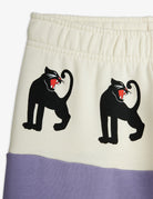 Close-up of a garment showing an off-white upper section with two black panther graphics holding red flags, and a lavender-purple lower band.