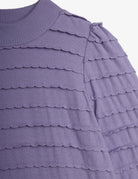 Close-up of a lavender purple knit top with horizontal scalloped ruffle details and a ribbed crew neck.