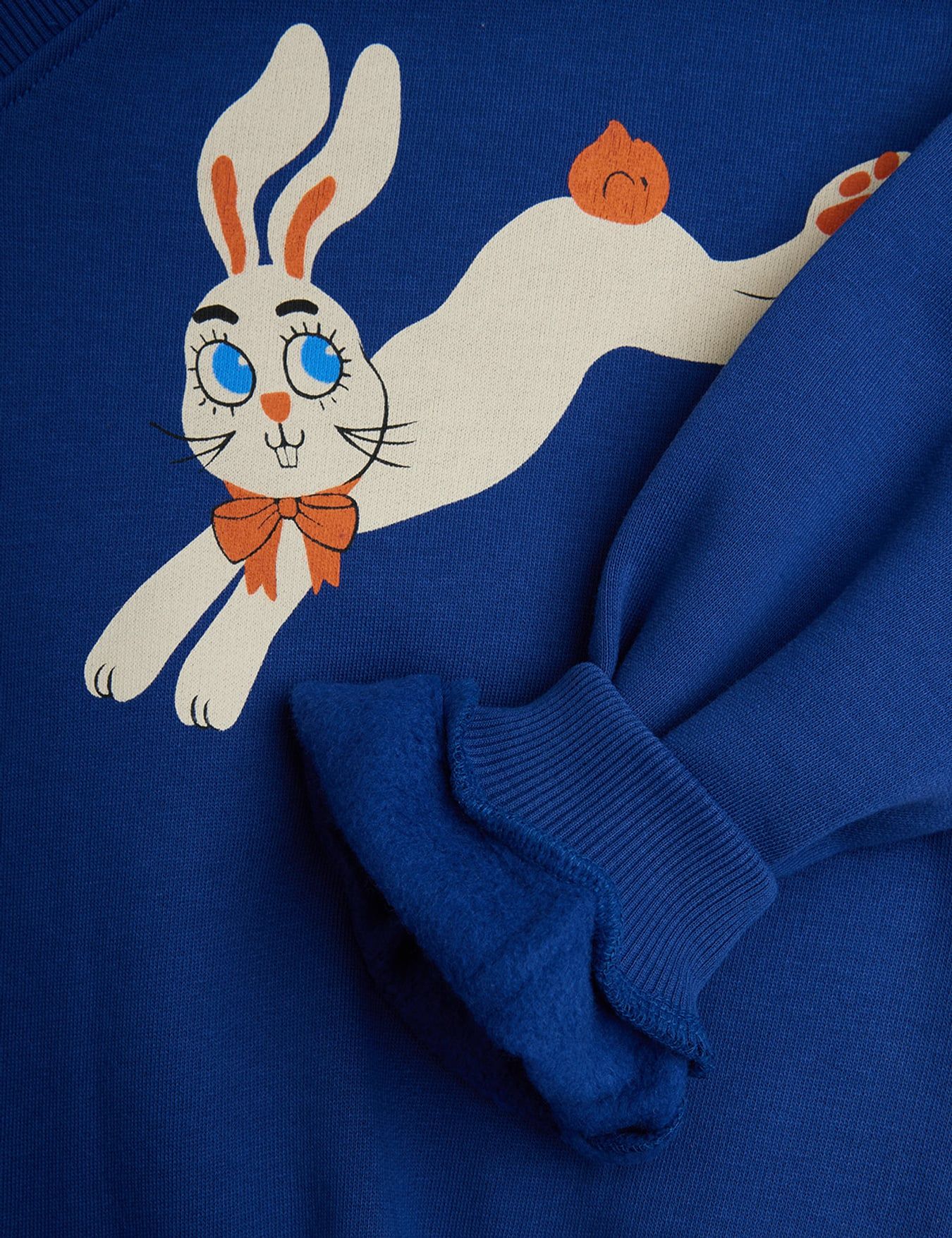 A close-up of a royal blue sweatshirt featuring a cartoon graphic of a white rabbit with blue eyes, orange ears, and an orange bow tie.