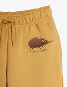 Close-up of mustard yellow sweatpants featuring a brown embroidered elephant shrew on the left leg with the text 'ELEPHANT SHREN' beneath it, shown against a plain white background.