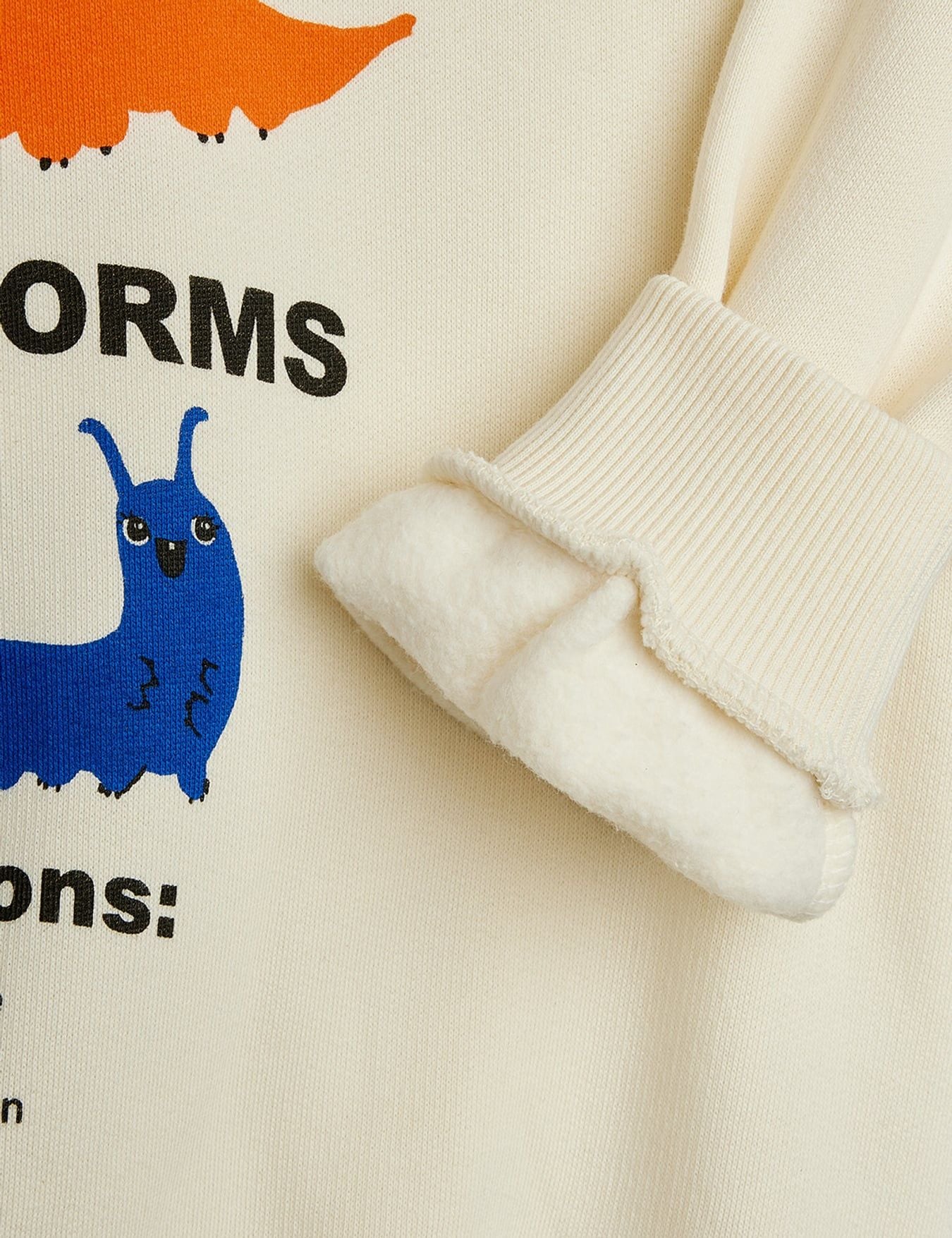 Close-up of a cream-colored fleece-lined sweatshirt showing the ribbed cuff and a colorful cartoon worm graphic with black text.