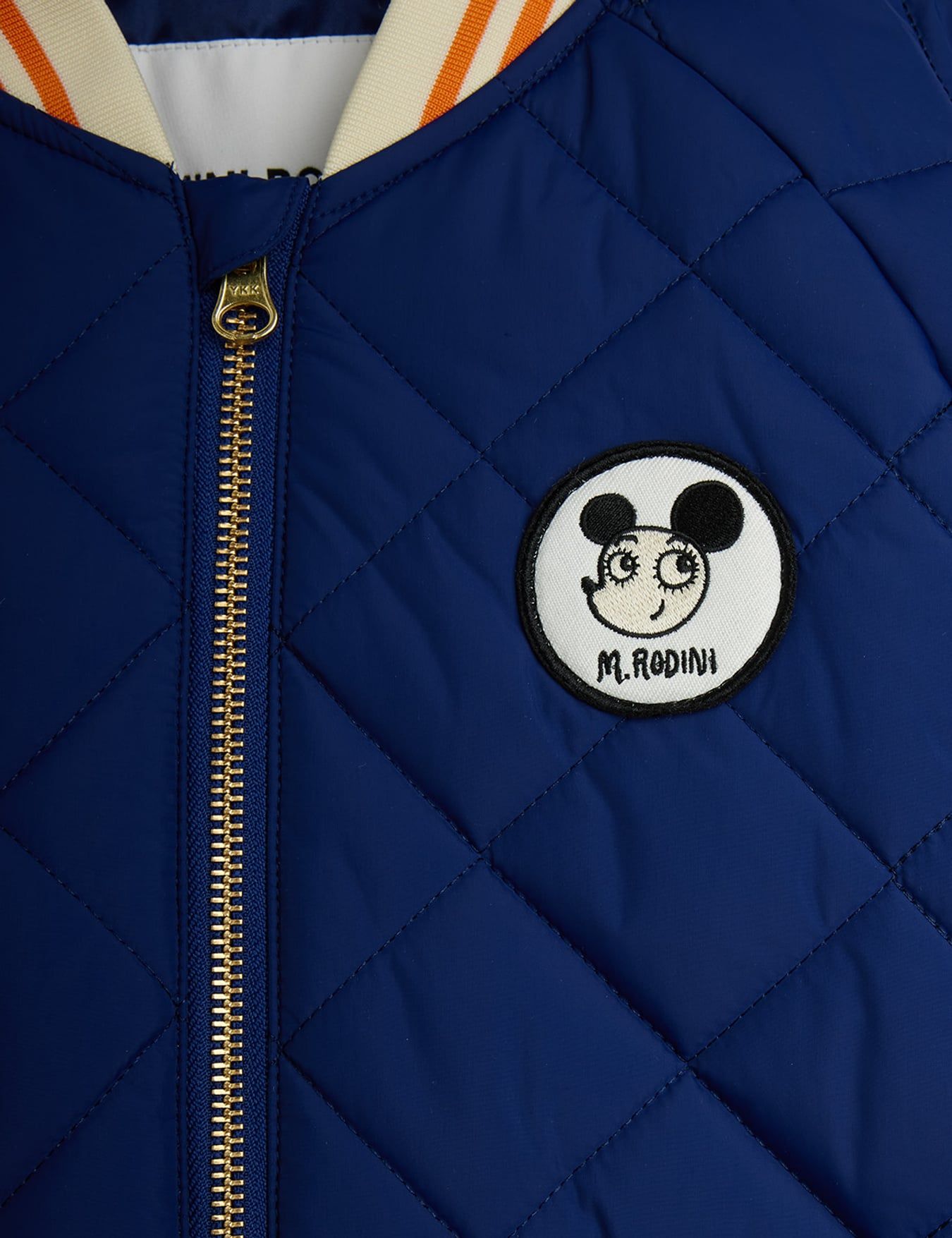 Close-up of a quilted navy blue puffer jacket showing a diamond-stitched pattern and a front pocket with an elasticated opening.