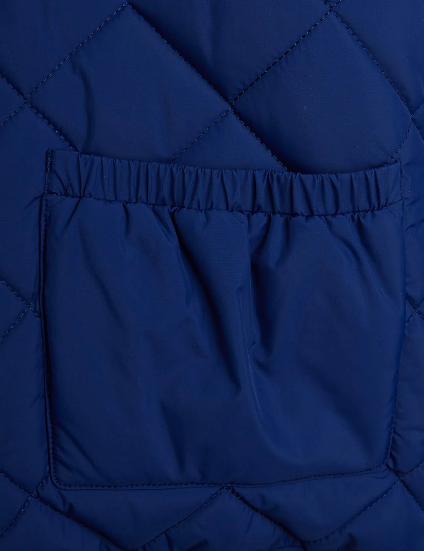 Close-up of a quilted navy blue puffer jacket showing a diamond-stitched pattern and a front pocket with an elasticated opening.