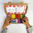 Colorful bead set in an open cardboard box with hands interacting with the beads on a light background