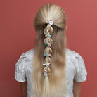 Person with long blonde hair styled in braids with decorative hair clips against a red background