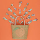 Woven bag with peach design and decorative hair clips on an orange background